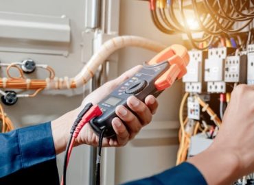 Electrician engineer uses a multimeter to test the electrical installation and power line current in an electrical system control cabinet.
